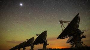 An image of the Very Large Array at night, with the large radio antenna dishes silhouetted against a starry background.