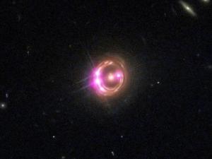 The four bright magenta points are images of a single quasar, magnified and multiplied by the gravity of the galaxy.